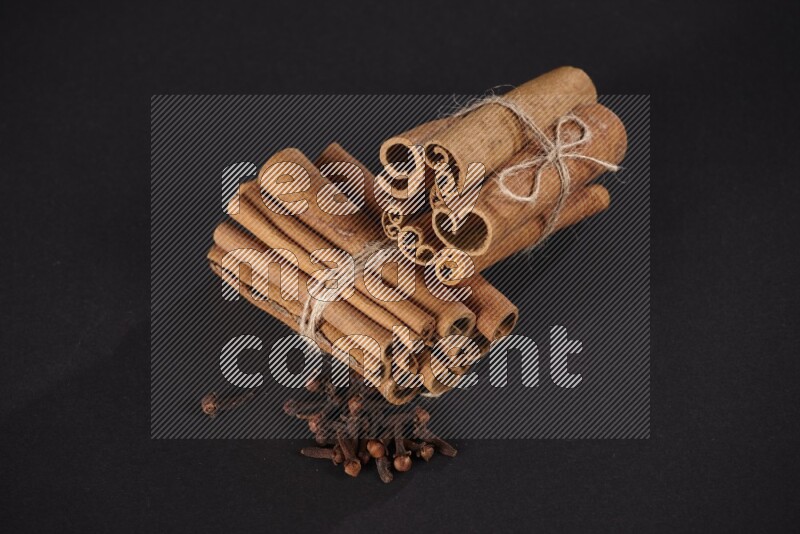 Two bounded stacks of cinnamon sticks with cloves on black background