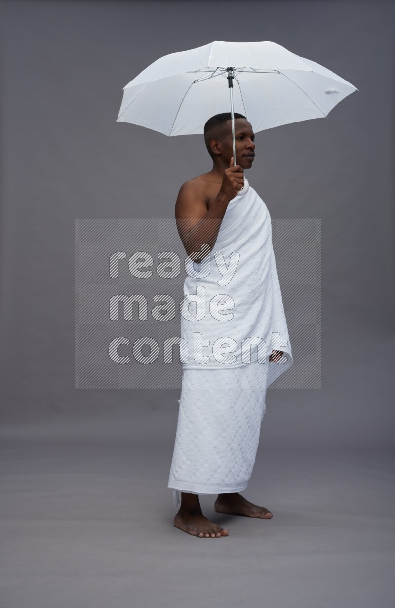 A man wearing Ehram Standing holding umbrella on gray background