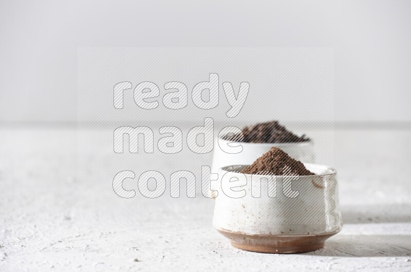 2 Beige ceramic bowls, one full of cloves and the other full of powder on textured white flooring