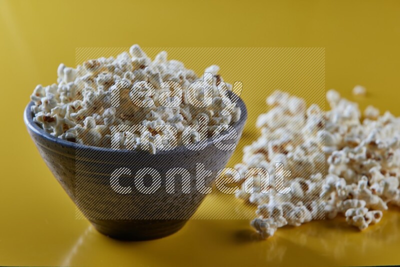 A multicolored pottery bowl full of popcorn with popcorn beside it on a yellow background in different angles