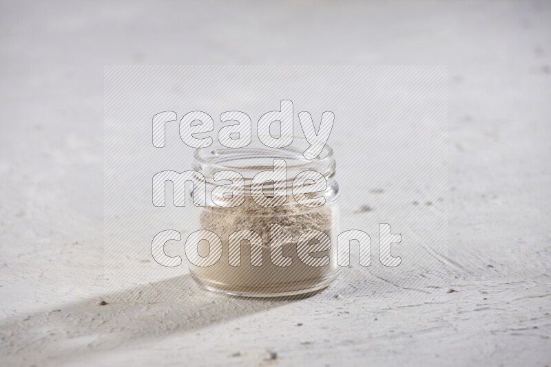 A glass jar full of garlic powder on a textured white flooring