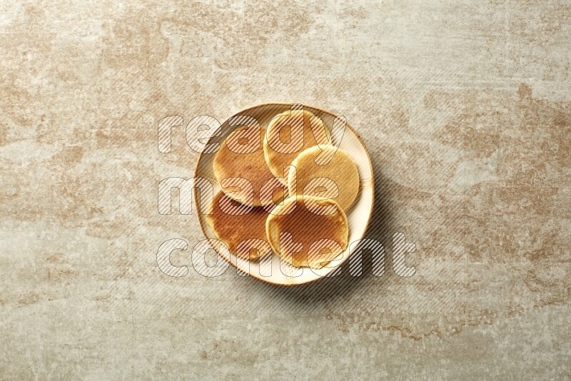 Five stacked plain mini pancakes in an irregular plate on beige background