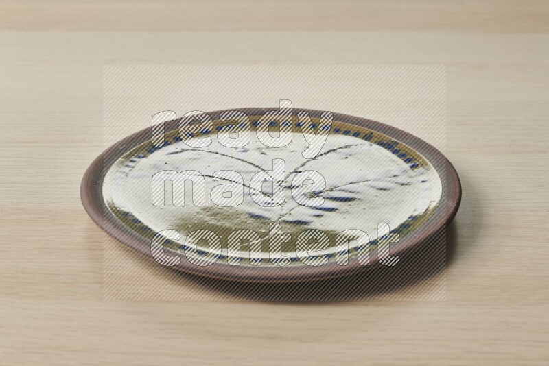 A decorative pottery plate on light wooden background