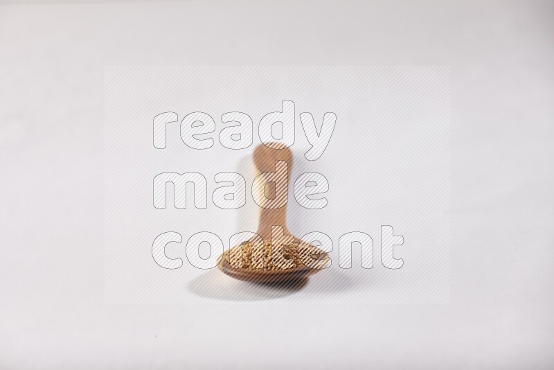 A wooden ladle full of mustard seeds on a white flooring