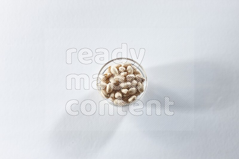 A glass bowl full of pistachios on a white background in different angles
