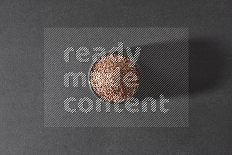 A black pottery bowl full of flaxseeds on a black flooring