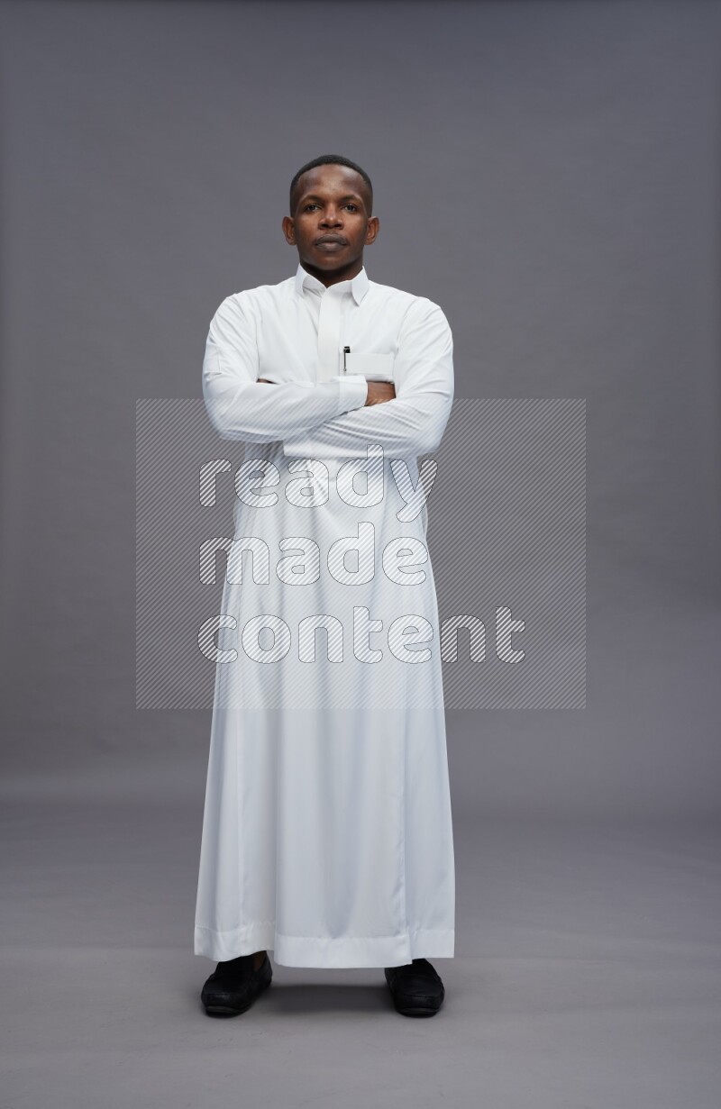 Saudi man wearing thob standing with crossed arms on gray background