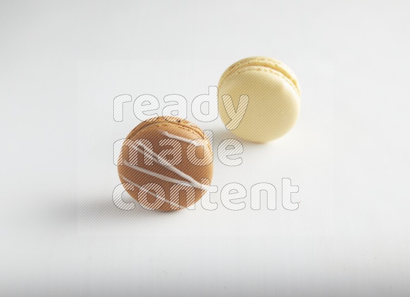 45º Shot of of two assorted Brown Irish Cream, and Yellow Vanilla macarons on white background