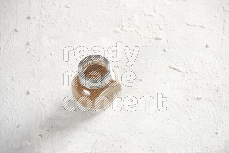 Herbs glass jar full of cinnamon powder on a textured white background