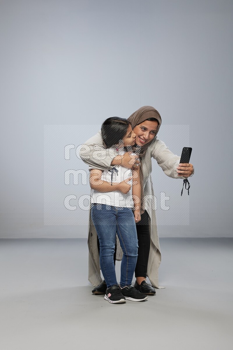 A girl standing taking selfie with her mother on gray background