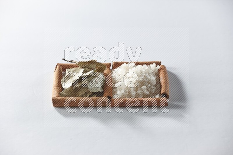 مربعان من أعواد القرفة ممتلئان بالملح الأبيض وأوراق الغار علي خلفية بيضاء