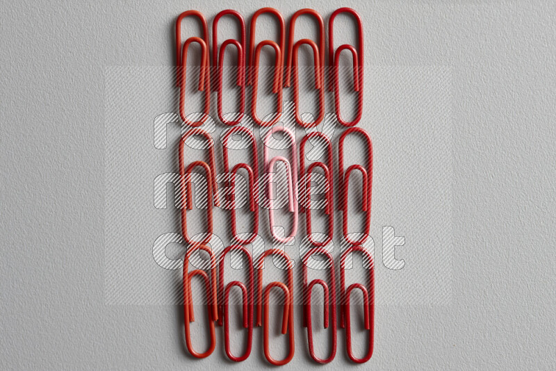 A bunch of red paper clips with a different colored paper clip in the center on grey background