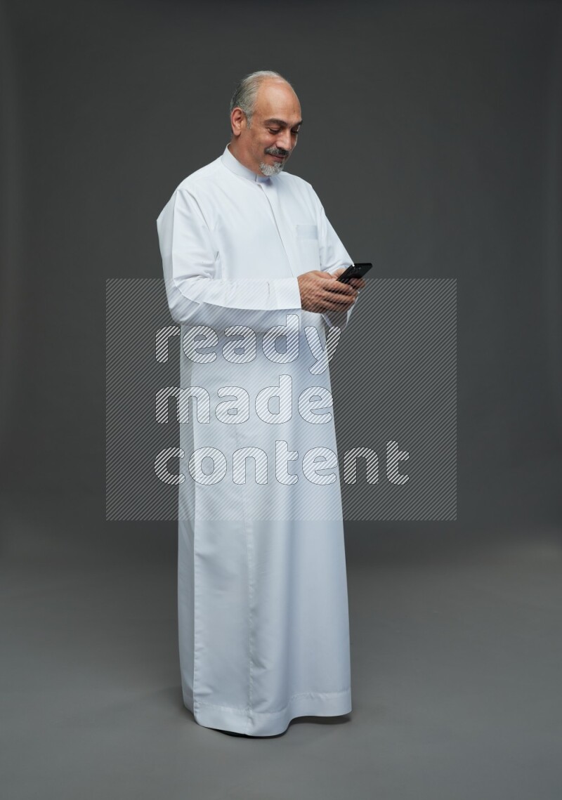 Saudi man without shomag Standing texting on phone on gray background