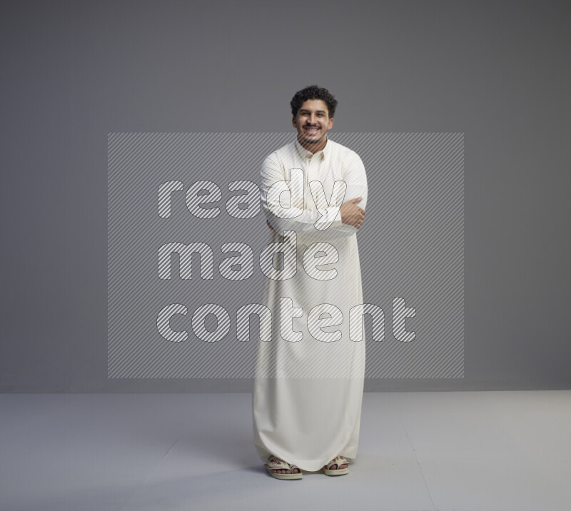 A Saudi man standing wearing thob interacting with the camera on gray background