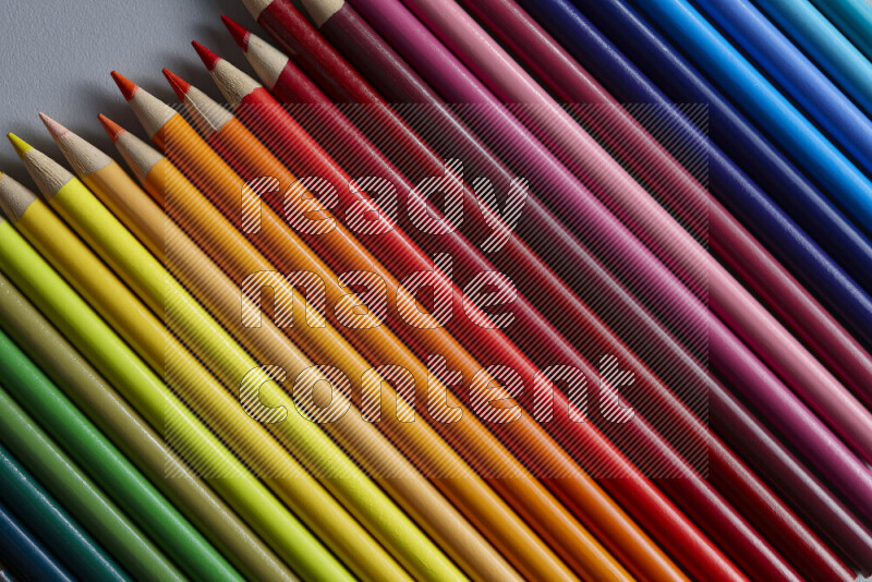 A collection of colored pencils arranged showcasing a gradient of different hues on grey background