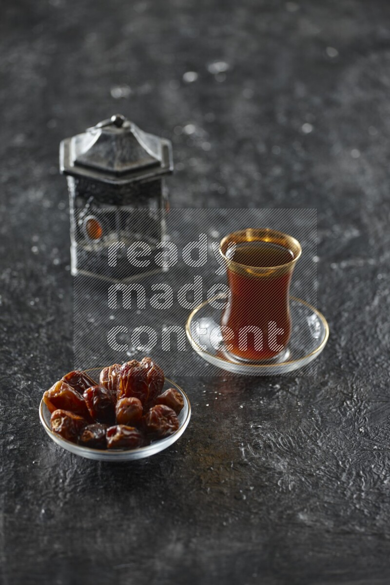 A silver lantern with different drinks, dates, nuts, prayer beads and quran on textured black background