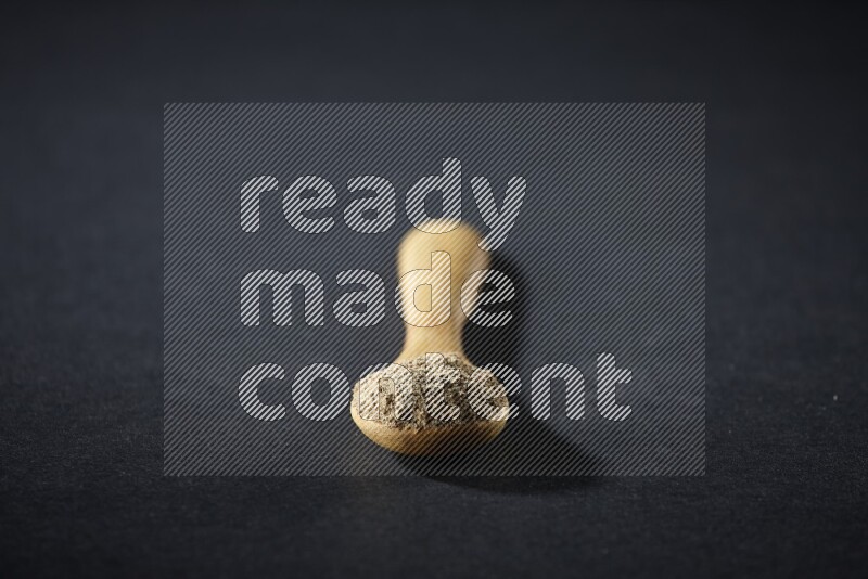 A wooden spoon full of cardamom powder on black flooring