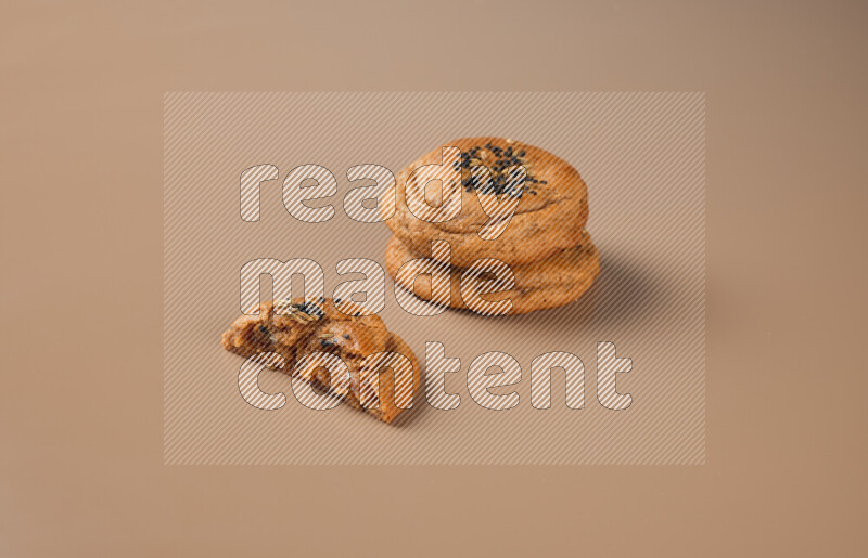 Two Hasawi cookies field of date and decorated by black seed and anise grain with another one cut in half on a brown background
