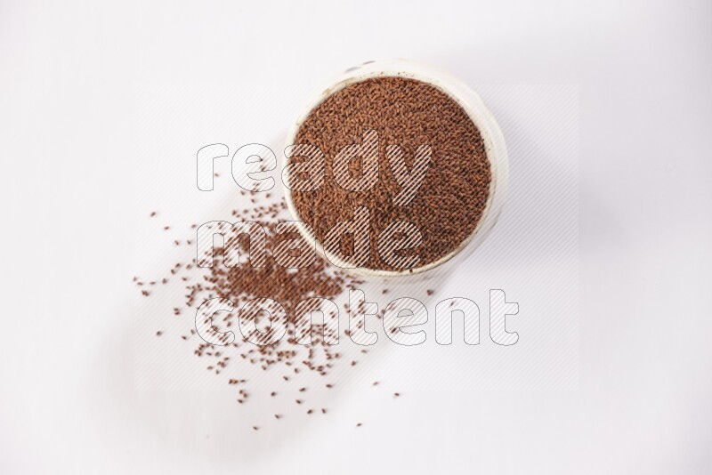 A beige pottery bowl full of garden cress seeds with more seeds spread on a white flooring