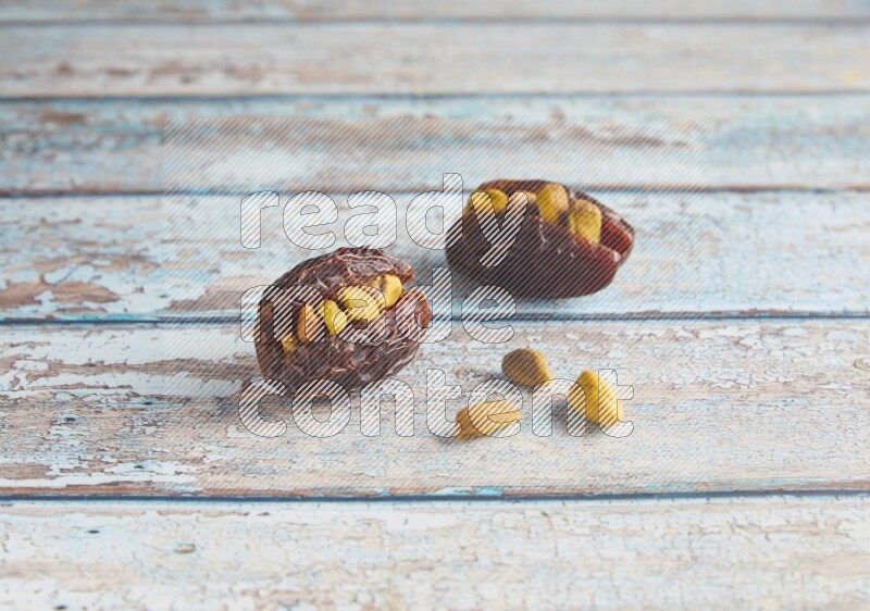 two pistachio stuffed madjoul dates on a light blue wooden background
