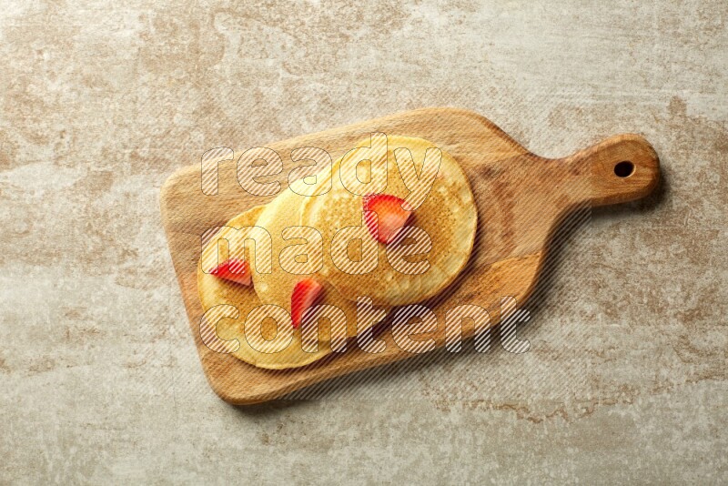Three stacked strawberry pancakes on a wooden board on beige background