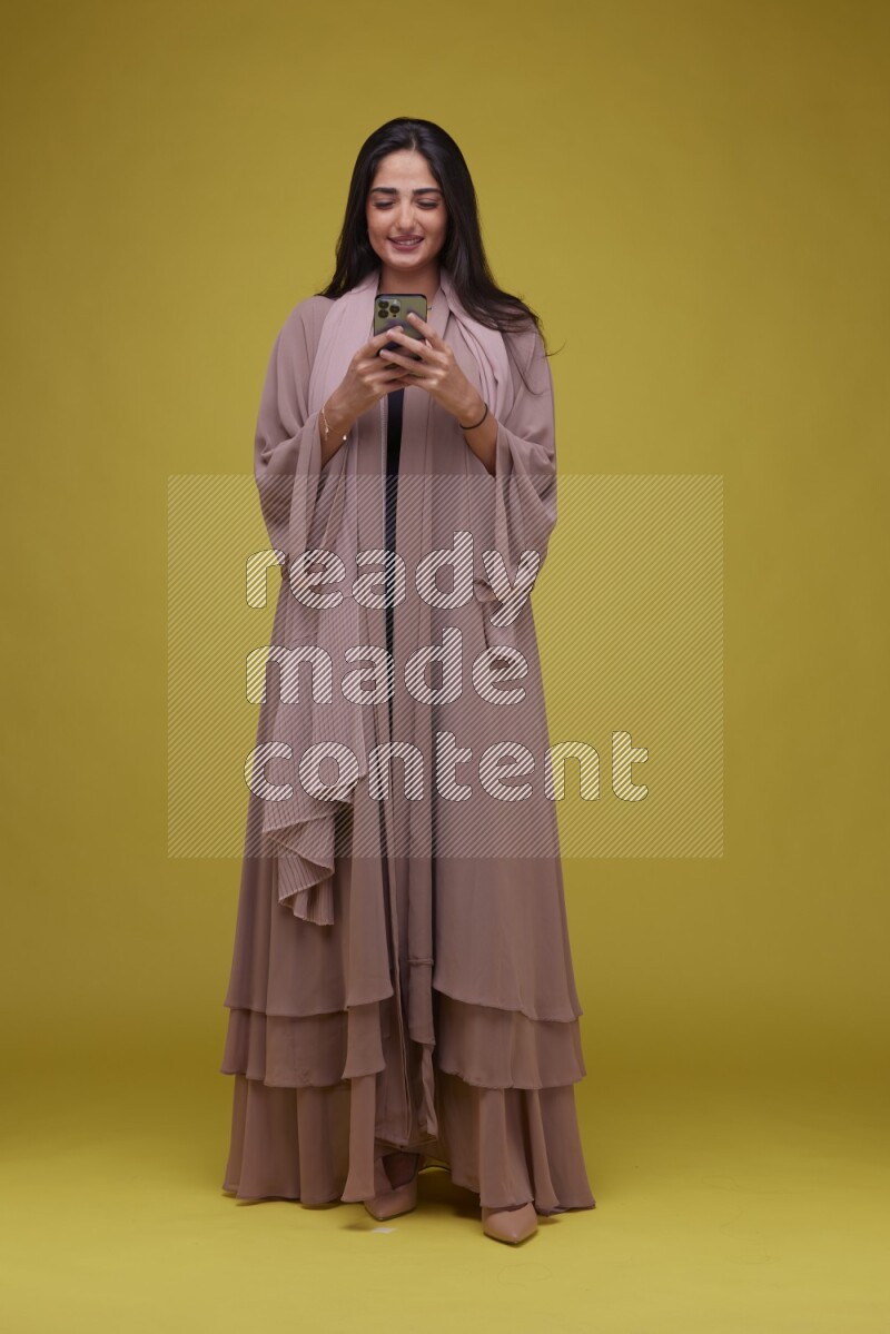 A woman Texting on a Yellow Background wearing Brown Abaya