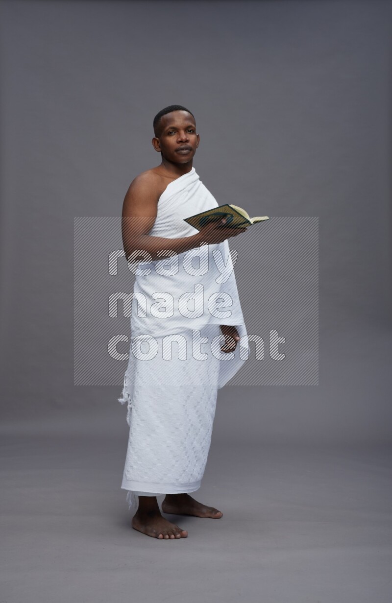 A man wearing Ehram Standing reading quran on gray background