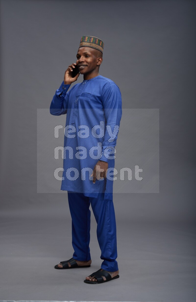 Man wearing Nigerian outfit standing talking on phone on gray background