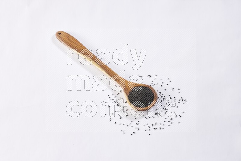A wooden ladle full of black seeds on a white flooring