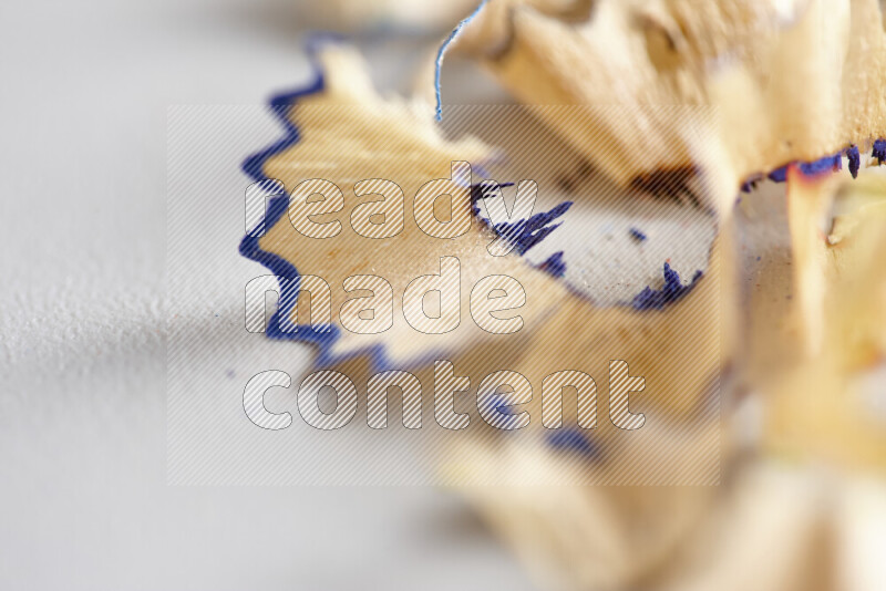 A close-up showing a small pile of pencil shavings with varied color edges on grey background