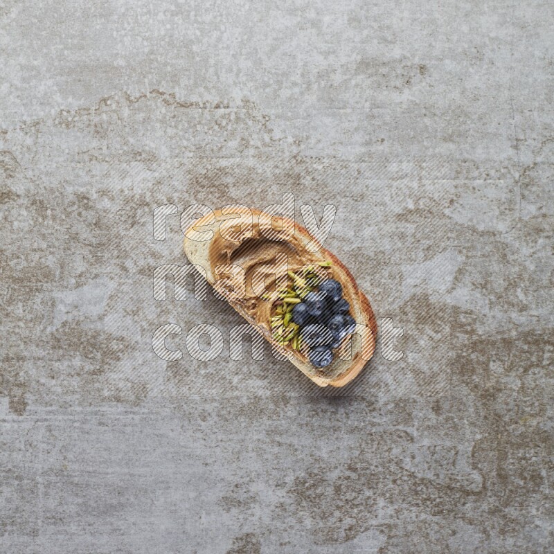 open faced peanut butter sandwich with blueberries and pistachio on a grey textured background