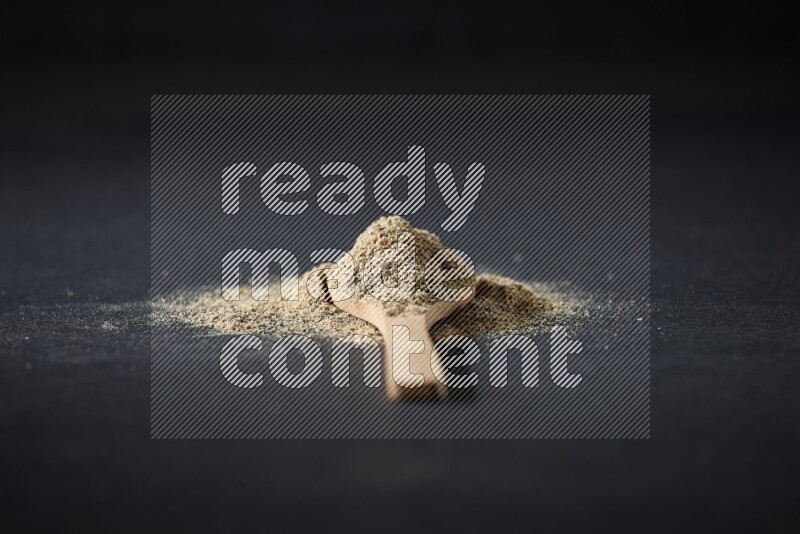 A wooden spoon full of cardamom powder and powder spreaded on black flooring
