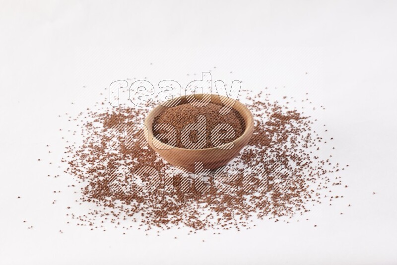 A wooden bowl full of garden cress seeds with more seeds spread on a white flooring
