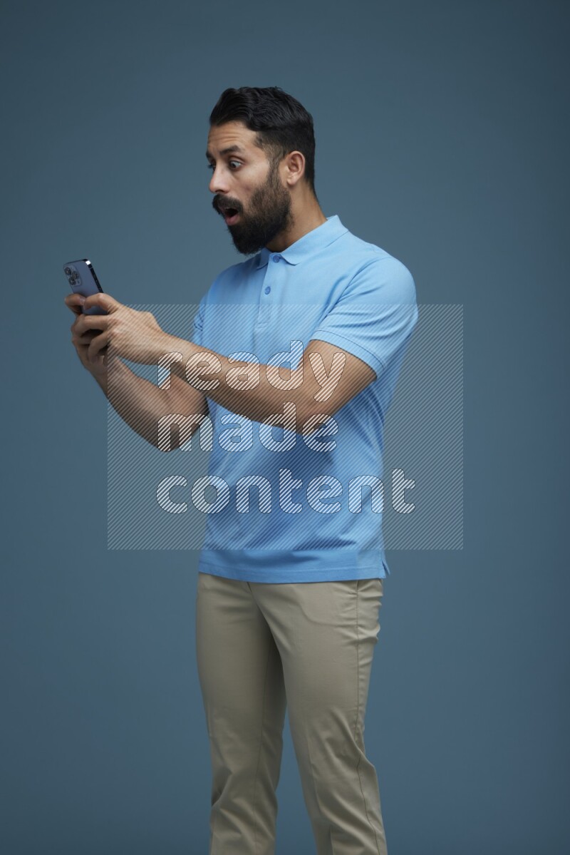A man Texting on his phone in a blue background wearing a Blue shirt