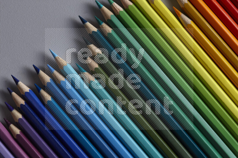 A collection of colored pencils arranged showcasing a gradient of different hues on grey background