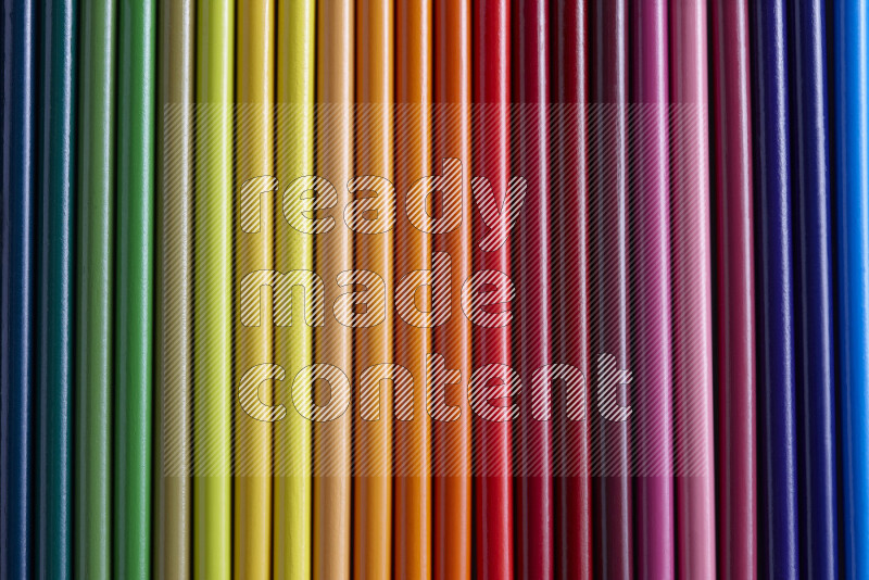 A collection of colored pencils arranged showcasing a gradient of different hues on grey background