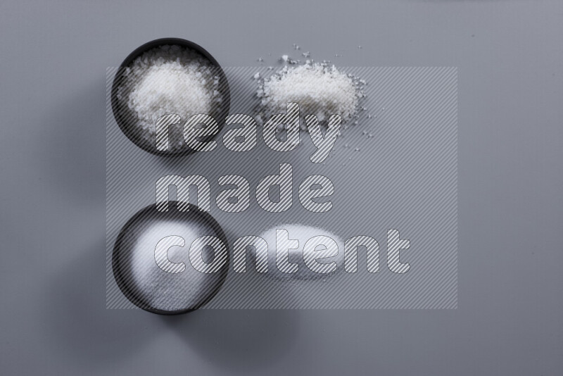 2 pottery bowls one is filled with table salt and the other with coarse sea salt on grey background