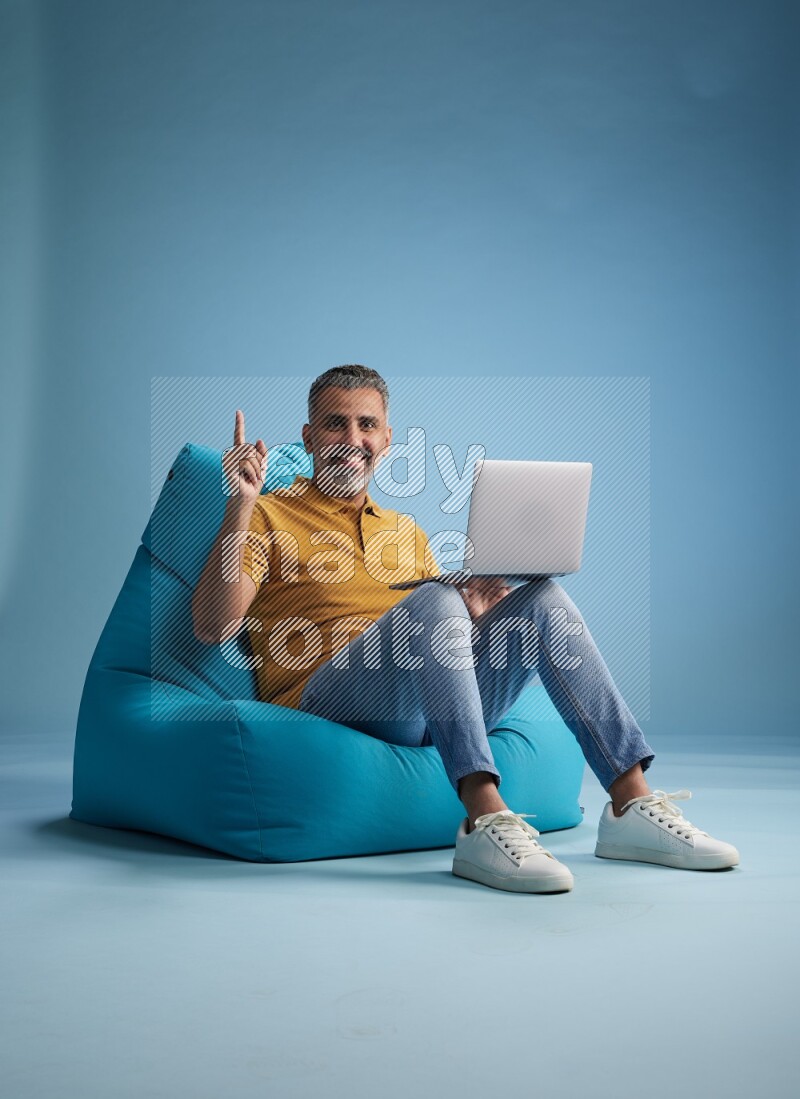 A man sitting on a blue beanbag and working on laptop