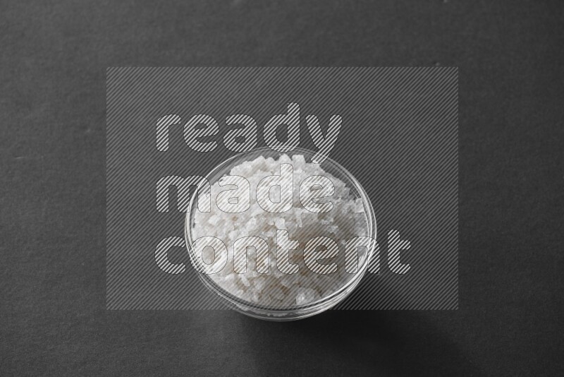 A glass bowl full of salt on black flooring