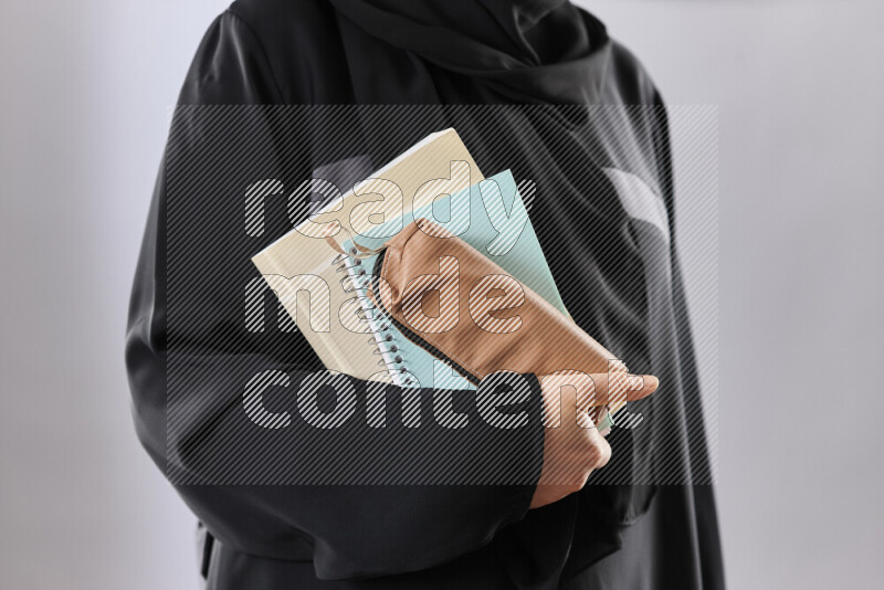 A woman in abaya holding books and a board in different positions (back to school)
