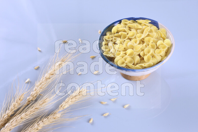 Raw pasta with wheat stalks on light blue background