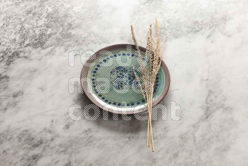 Wheat stalks on decorative pottery plate on grey marble background