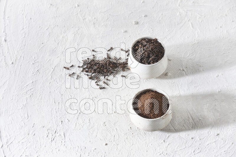 2 Beige ceramic bowls, one full of cloves and the other full of powder on textured white flooring