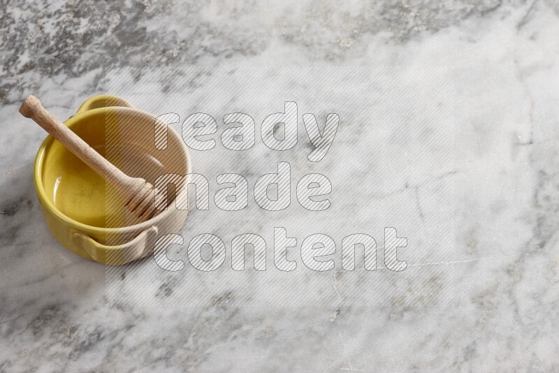 وعاء فخاري متعدد الألوان مع ملعقة عسل خشبية بداخله على خلفية من الرخام الرمادي