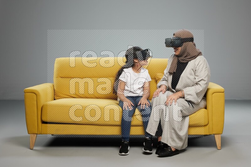 A girl and her mother sitting playing with VR on gray background