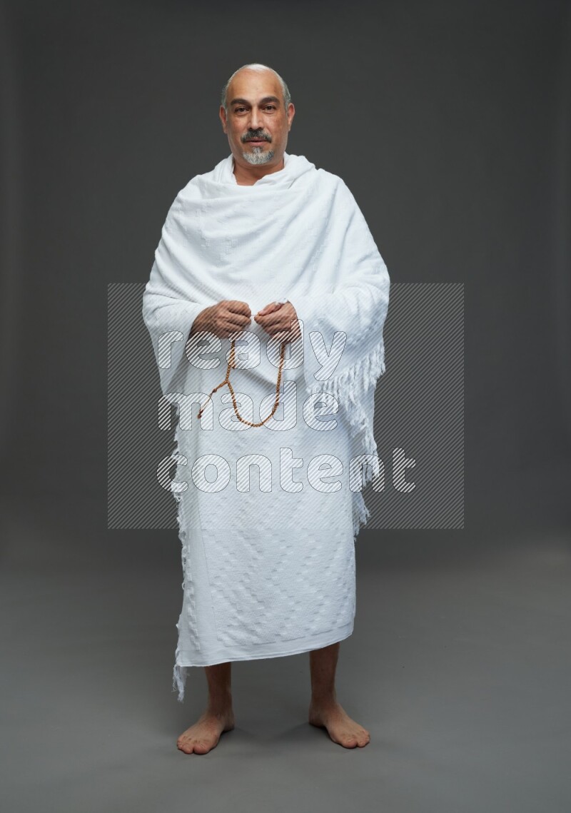 A man wearing Ehram Standing holding rosary on gray background
