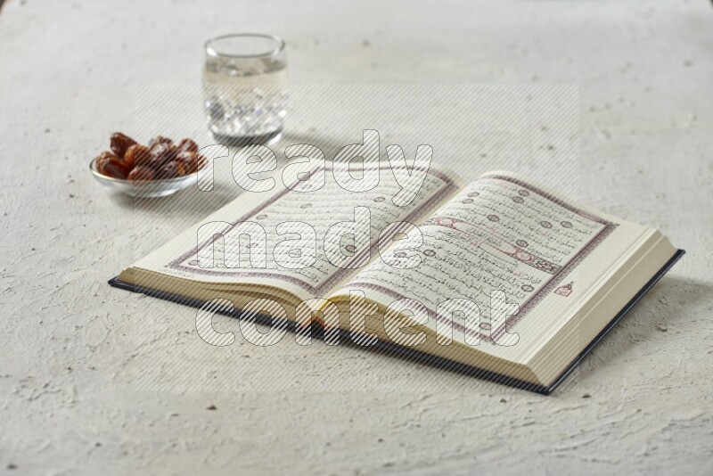 Quran with dates, prayer beads and different drinks all placed on textured white background