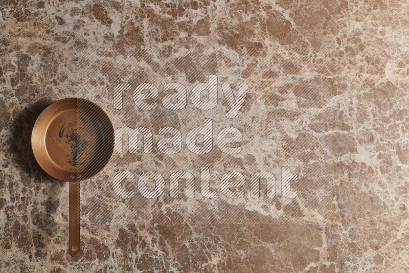 A small copper pan on beige marble background