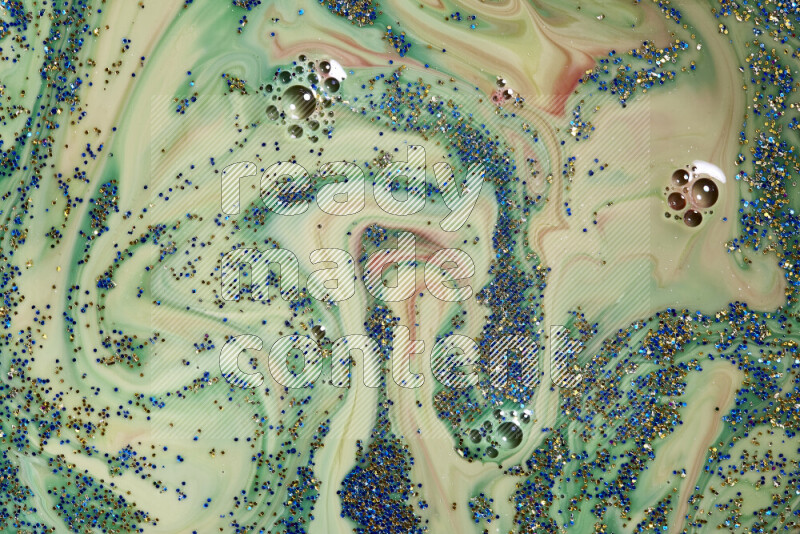 A close-up of sparkling blue and gold glitter scattered on swirling green and red background