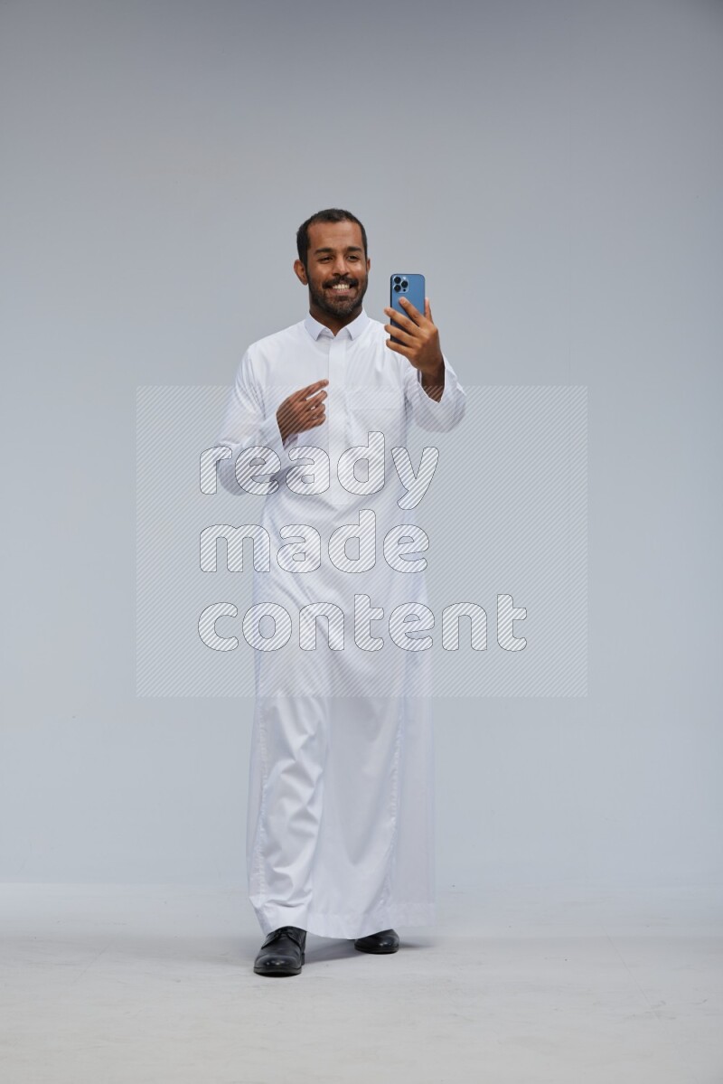 Saudi man wearing Thob standing taking selfie on Gray background